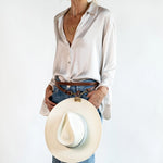 Waist style shown wearing the Sidecar The OG 14K gold hat clip with genuine brown leather side strap, white stitching, and adjustable leather strap with 14k hardware. Luxury, hands-free hat carry worn in 4 styles: Crossbody, Backpack, Purse-style, and Waist-wear.