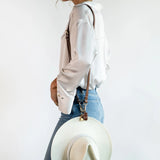 Purse-style shown wearing the Sidecar The OG 14K gold hat clip with genuine brown leather side strap, white stitching, and adjustable leather strap with 14k hardware. Luxury, hands-free hat carry worn in 4 styles: Crossbody, Backpack, Purse-style, and Waist-wear.