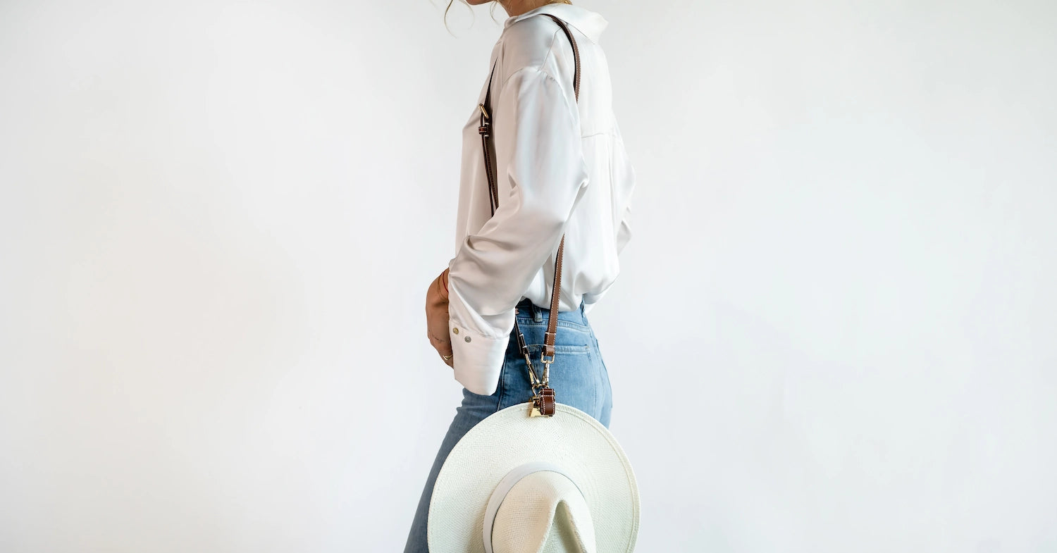 Purse-style shown wearing the Sidecar The OG 14K gold hat clip with genuine brown leather side strap, white stitching, and adjustable leather strap with 14k hardware. Luxury, hands-free hat carry worn in 4 styles: Crossbody, Backpack, Purse-style, and Waist-wear.