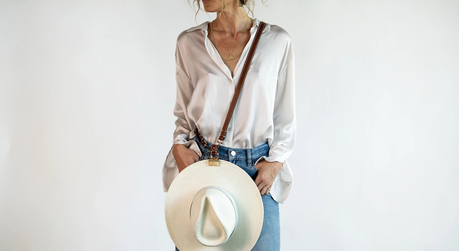 Crossbody Style shown wearing the Sidecar The OG 14K gold hat clip with genuine brown leather side strap, white stitching, and adjustable leather strap with 14k hardware. Luxury, hands-free hat carry worn in 4 styles: Crossbody, Backpack, Purse-style, and Waist-wear.