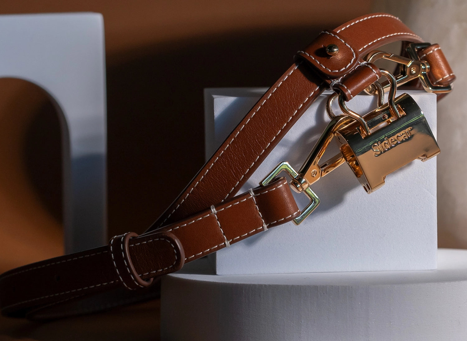 Sidecar The OG 14K gold hat clip with genuine brown leather side strap, white stitching, and adjustable leather strap with 14k hardware. Luxury, hands-free hat carry worn in 4 styles: Crossbody, Backpack, Purse-style, and Waist-wear.