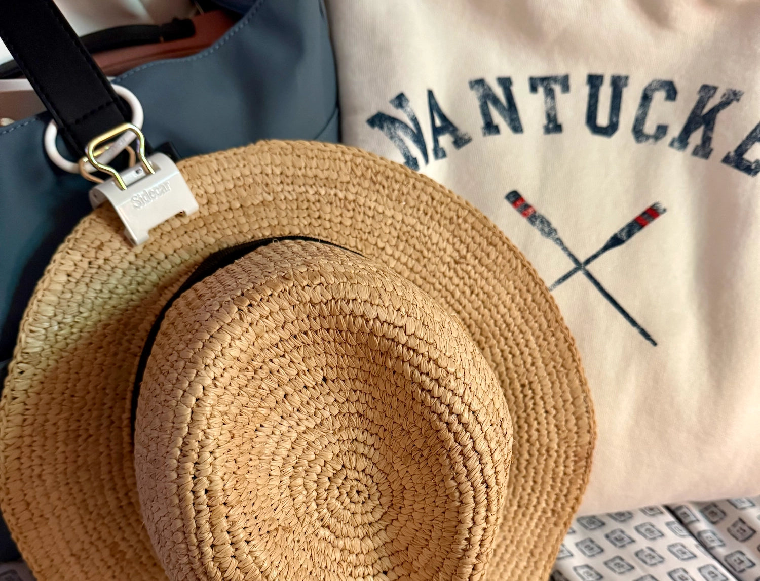 Close up of Sidecar classic white duo set with 14K gold hardware on woven hat attached to bag. Sidecar White Duo Set bundle with patented hat clips in white, featuring matching oval hinge clasps for hands-free hat carrying without bending or damage.